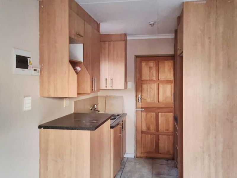 A compact kitchen featuring laminate cabinetry, stone countertops, a stainless steel sink, and tiled flooring, leading to a timber panel door.