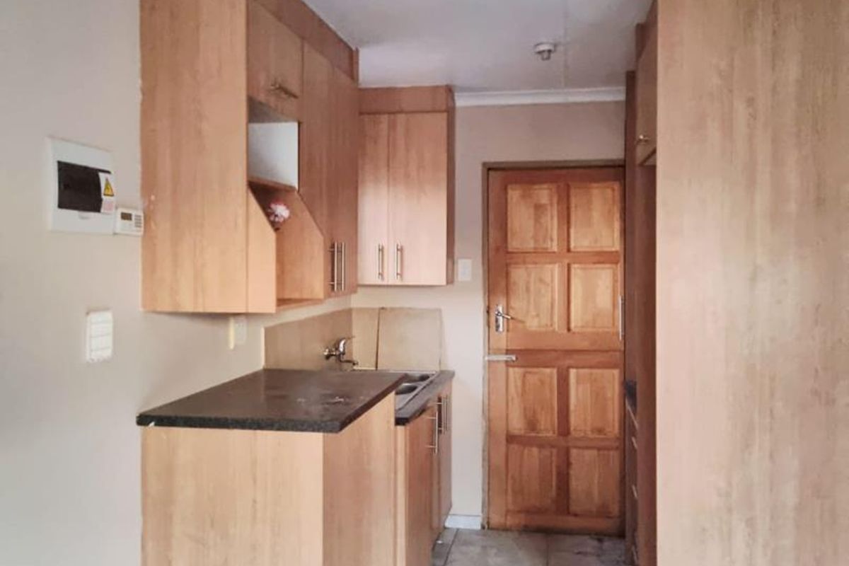 A compact kitchen featuring laminate cabinetry, stone countertops, a stainless steel sink, and tiled flooring, leading to a timber panel door.