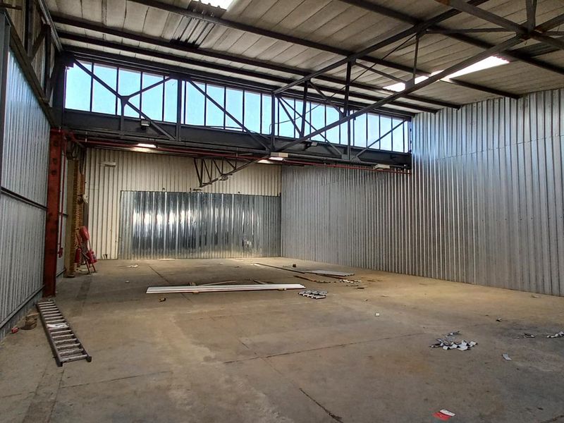 Spacious industrial warehouse unit featuring high ceilings with exposed steel trusses, corrugated metal walls, concrete flooring, and large clerestory windows for natural light.
