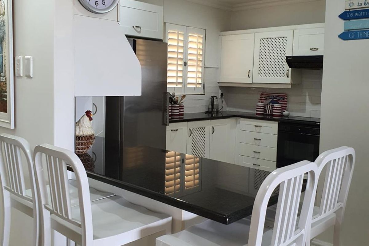 A well-maintained kitchen featuring white cabinetry, dark granite countertops, a breakfast bar, and integrated appliances, creating a functional and bright cooking space.