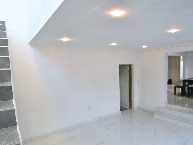 An open-plan living area featuring marble-look floor tiles, recessed ceiling lighting, and a tiled staircase leading to an upper level.