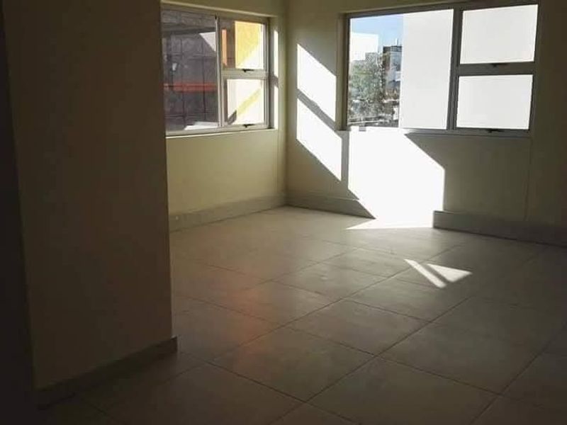 A bright, empty office space featuring neutral tiled flooring and large windows providing ample natural light.