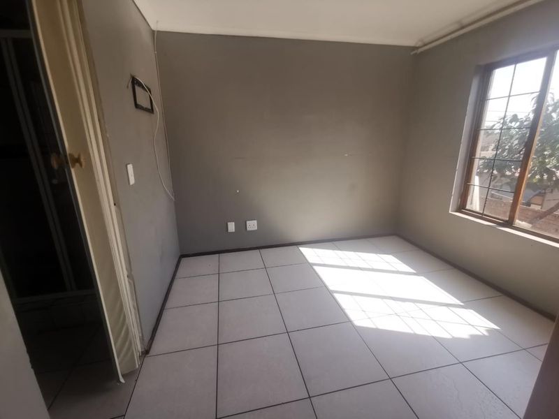 An empty bedroom featuring tiled flooring, a window with security bars, and neutral grey walls, ready for personalization.