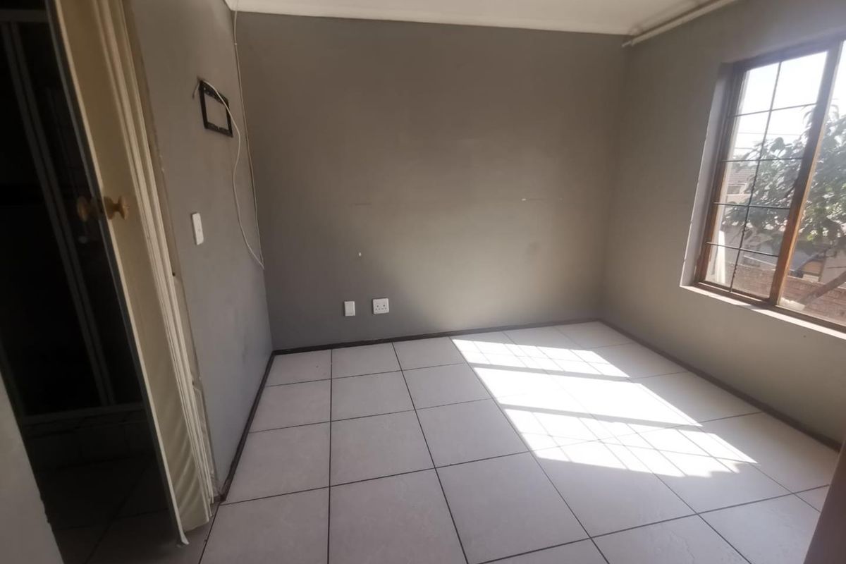 An empty bedroom featuring tiled flooring, a window with security bars, and neutral grey walls, ready for personalization.