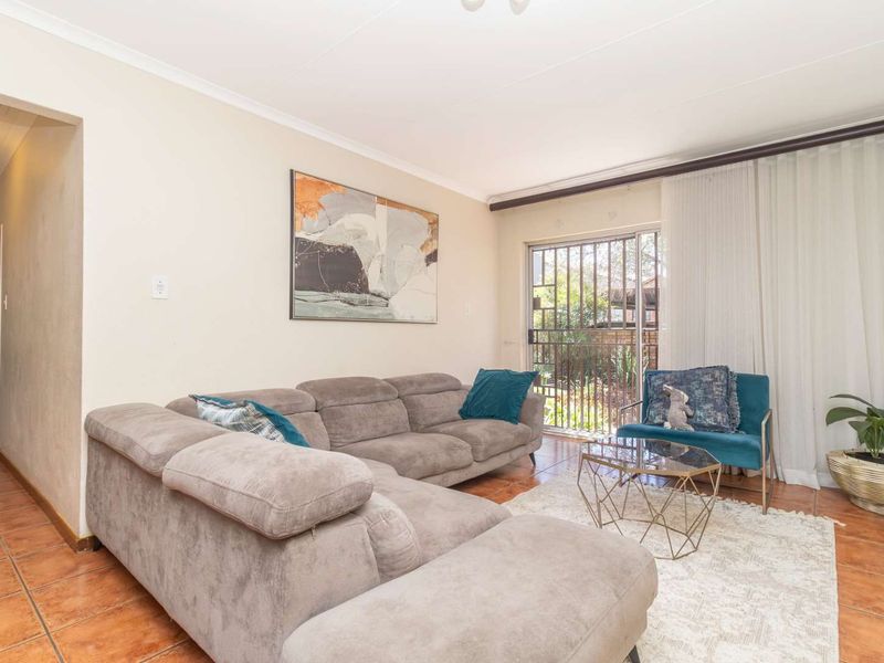 A comfortable living room featuring tiled flooring and a sliding glass door with security gate, providing access to the outdoor area.