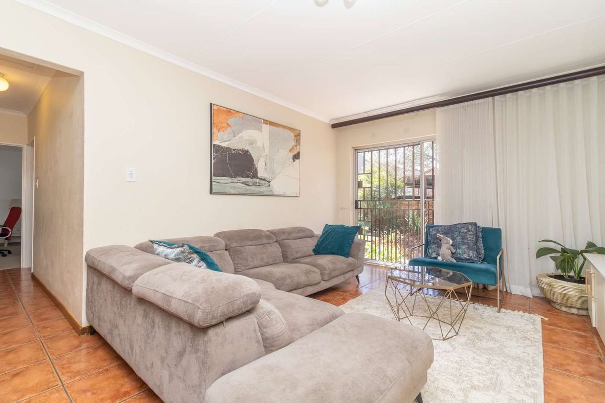 A comfortable living room featuring tiled flooring and a sliding glass door with security gate, providing access to the outdoor area.