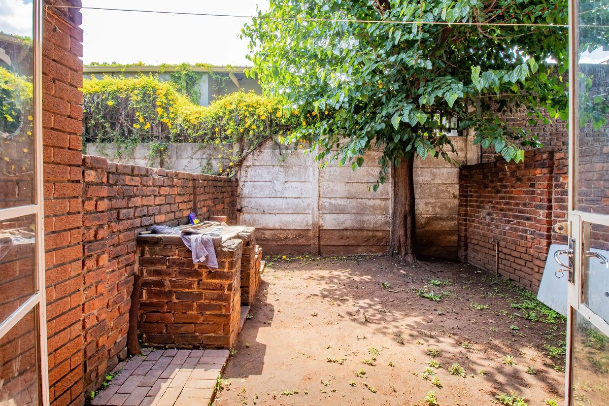 Private rear courtyard featuring a built-in brick braai, perimeter brick and concrete walls, and a mature tree, offering potential for landscaping.