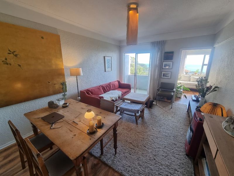Open plan living and dining area featuring laminate flooring and sliding glass doors leading to a balcony with natural light.