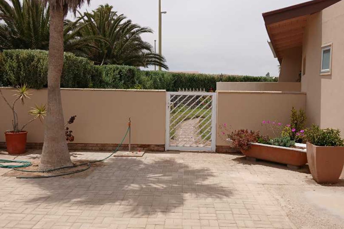 A paved rear courtyard area featuring a perimeter wall, a pedestrian gate, and established landscaping.