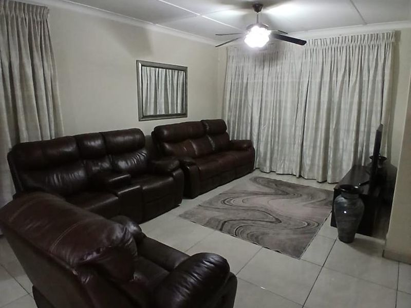 A living room featuring tiled flooring, a ceiling fan, and large windows covered by curtains.