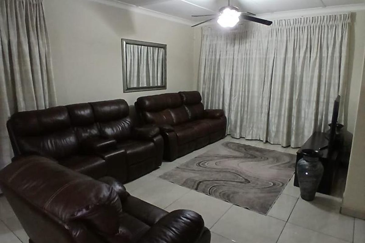 A living room featuring tiled flooring, a ceiling fan, and large windows covered by curtains.