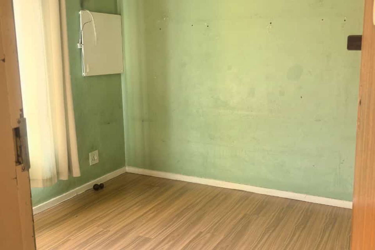 An empty bedroom featuring laminate flooring and a wall-mounted electric heater, requiring cosmetic updates and wall repairs.