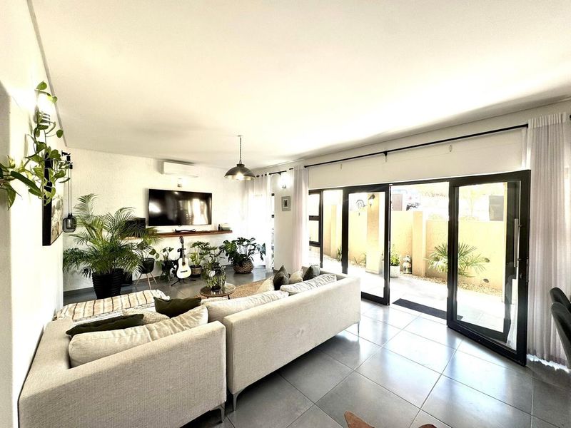 Bright and modern living room featuring large sliding glass doors that open to an outdoor area, tiled floors, and a wall-mounted air conditioning unit.