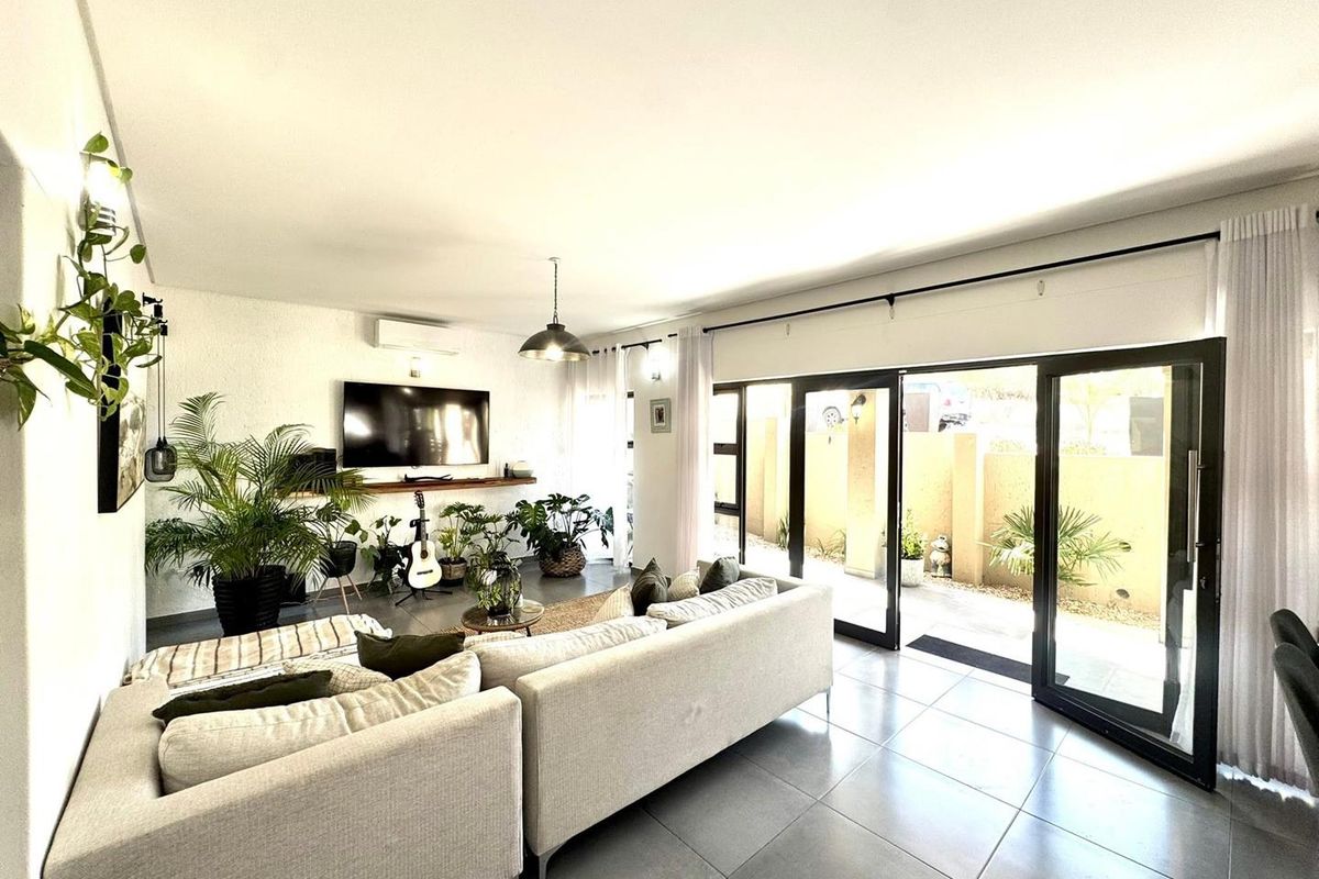 Bright and modern living room featuring large sliding glass doors that open to an outdoor area, tiled floors, and a wall-mounted air conditioning unit.