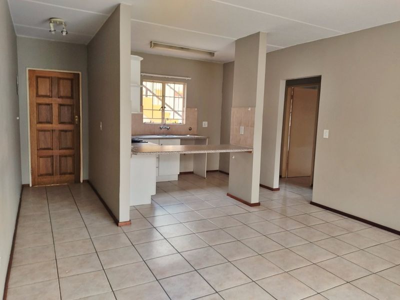 An open-plan living and kitchen area featuring neutral tiled flooring, a breakfast bar, and functional kitchen cabinetry in a clean, vacant space.