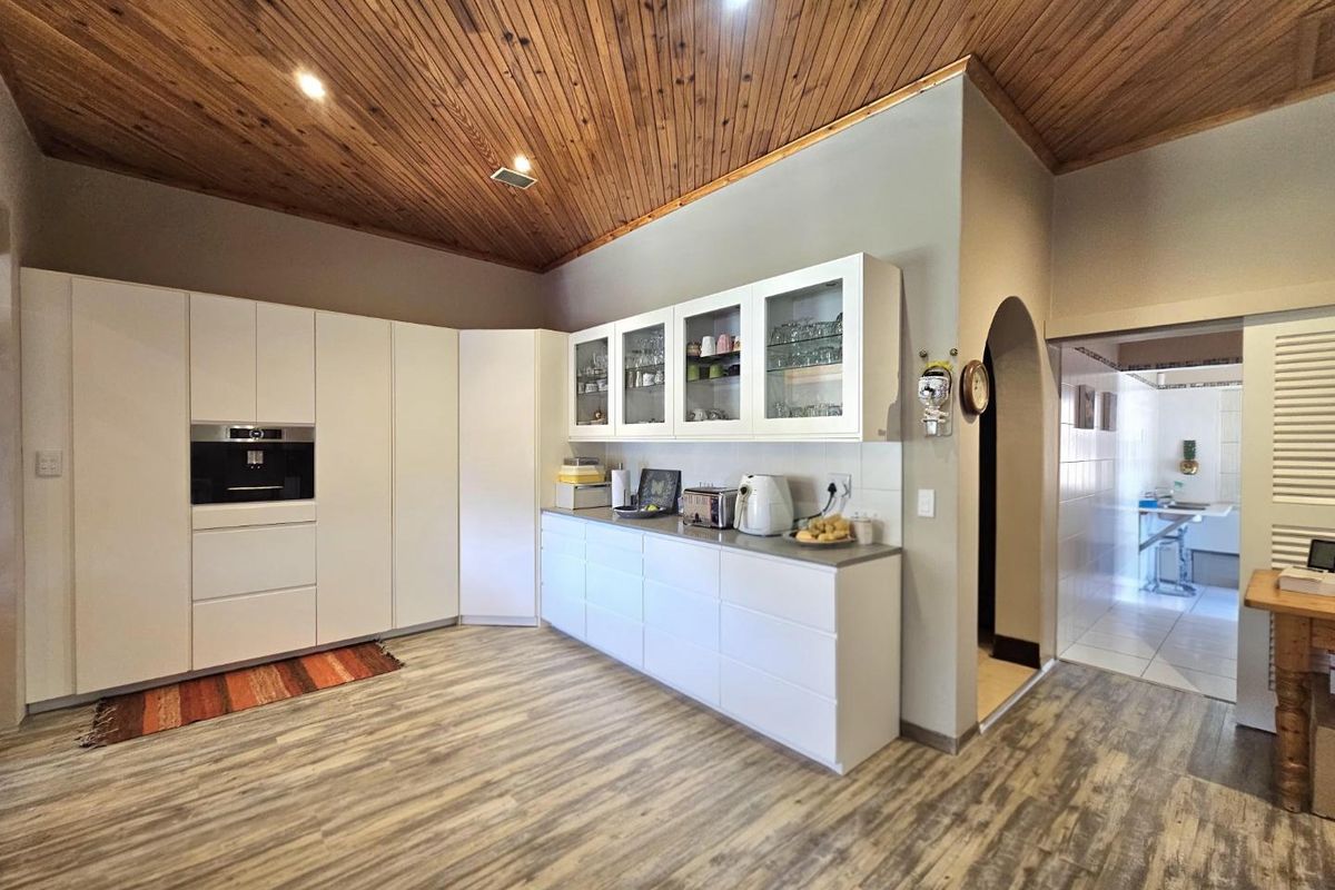 Modern kitchen featuring sleek white cabinetry, built-in oven, and a distinctive timber-clad vaulted ceiling, leading through an archway to an adjacent utility area.