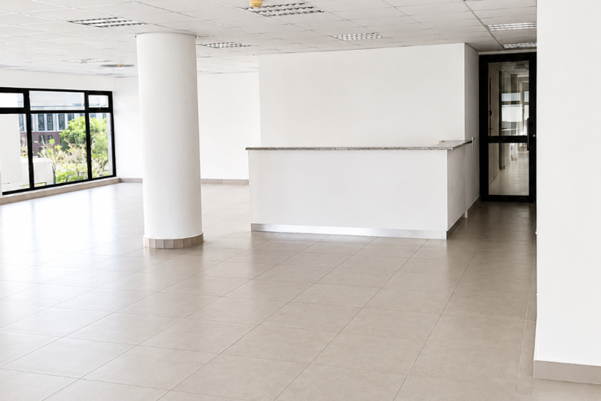Spacious open-plan office area featuring a built-in reception counter, neutral ceramic flooring, suspended ceilings, and large windows providing ample natural light.