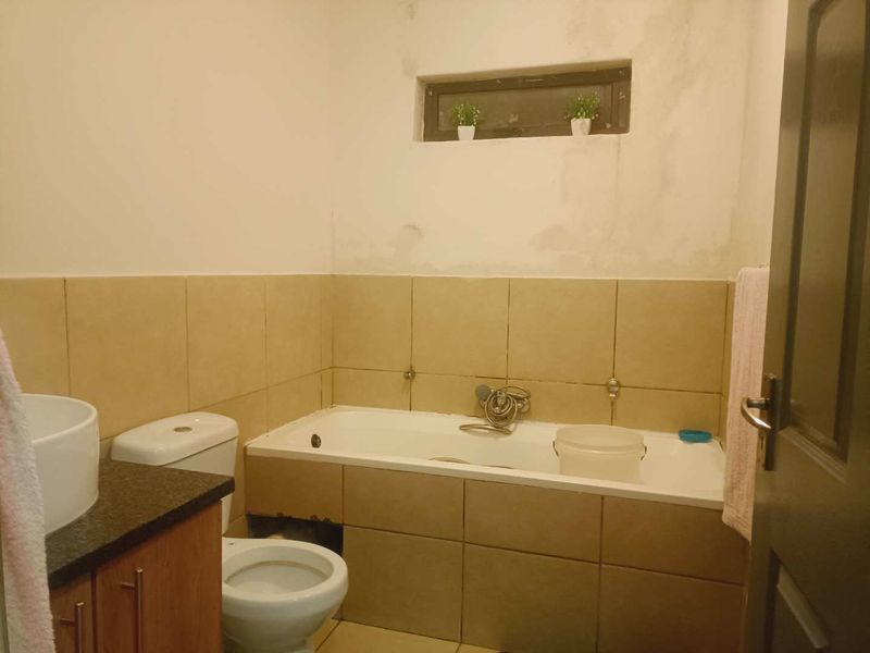 A functional bathroom featuring a bathtub, toilet, and vanity basin, currently requiring cosmetic attention to the wall finishes and bath paneling.