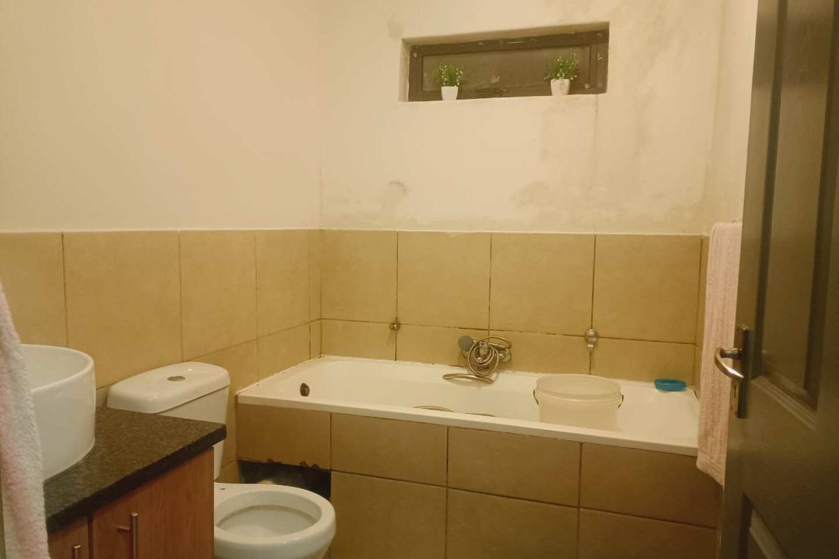 A functional bathroom featuring a bathtub, toilet, and vanity basin, currently requiring cosmetic attention to the wall finishes and bath paneling.
