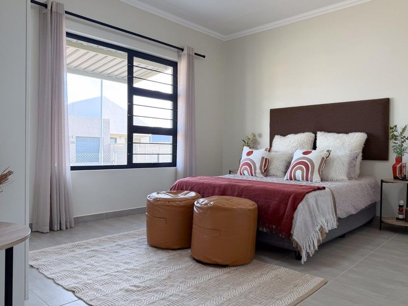 A well-maintained bedroom featuring neutral tiled flooring, clean wall finishes, and a large aluminium-framed window providing natural light.