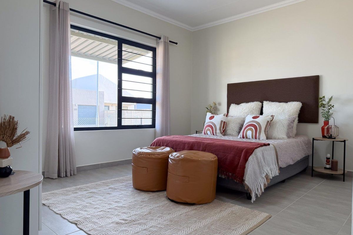 A well-maintained bedroom featuring neutral tiled flooring, clean wall finishes, and a large aluminium-framed window providing natural light.