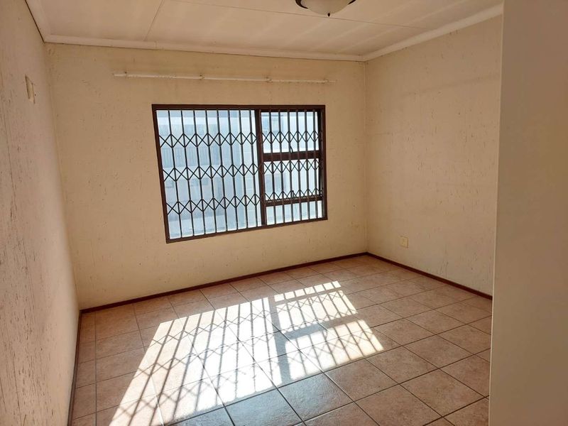 An empty bedroom featuring tiled flooring and security bars on the window, requiring cosmetic updates to the wall finishes.