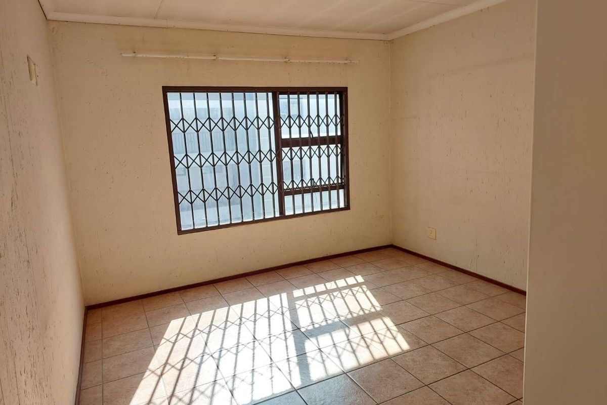 An empty bedroom featuring tiled flooring and security bars on the window, requiring cosmetic updates to the wall finishes.