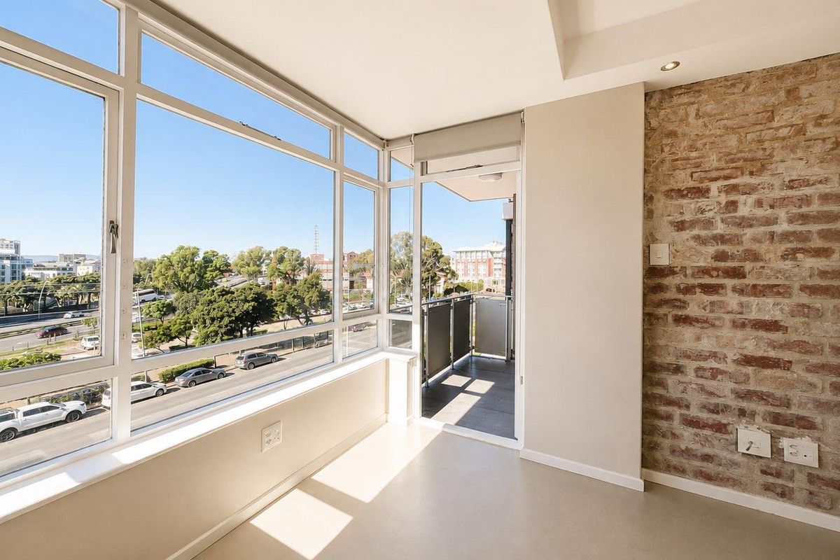 Bright and modern living area featuring an exposed brick wall, expansive windows with urban views, and direct access to a private balcony.