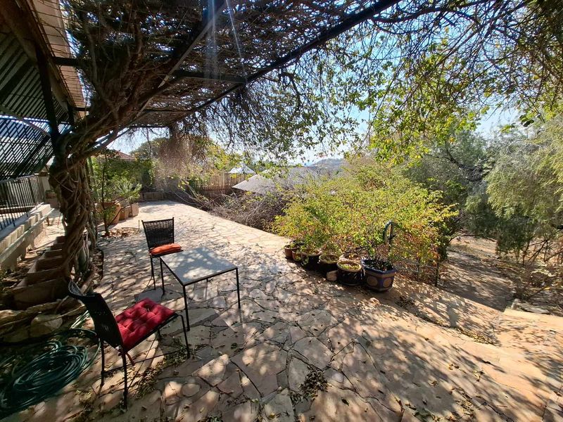 A covered outdoor patio area featuring stone paving and a metal pergola structure, overlooking a garden space.