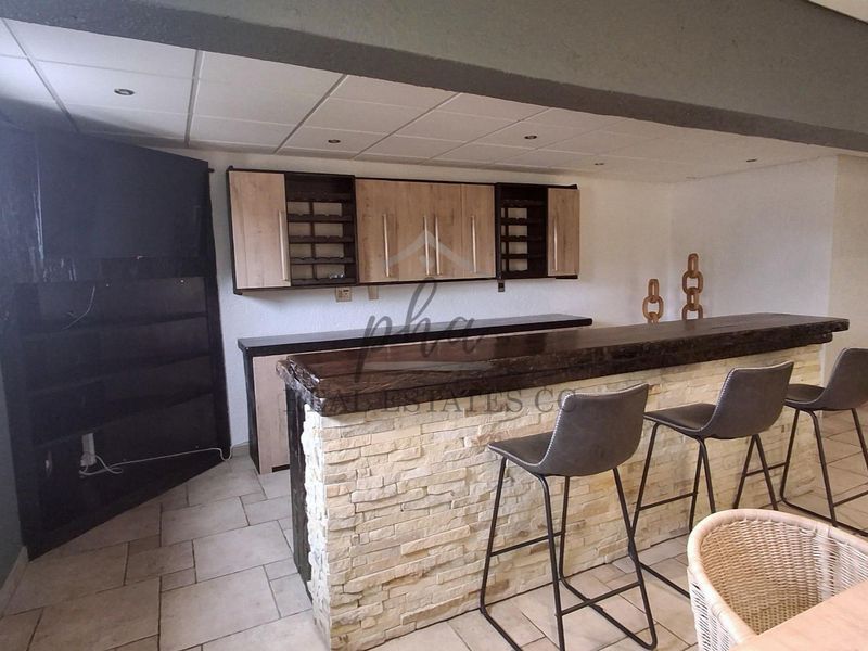 A dedicated bar area featuring a stone-clad counter with a wooden top, built-in cabinetry, and recessed ceiling lighting.