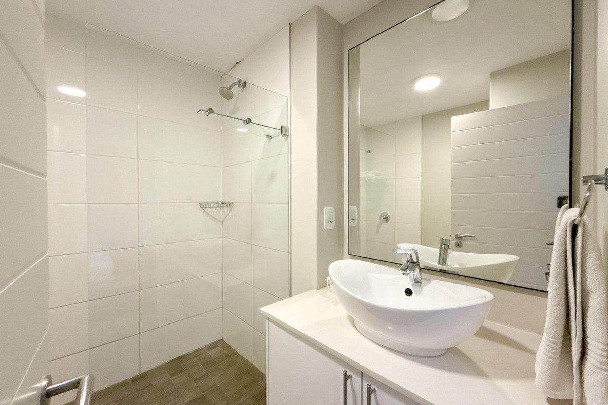Modern bathroom featuring a vessel sink vanity, large wall mirror, and a walk-in shower with a glass screen and white wall tiling.