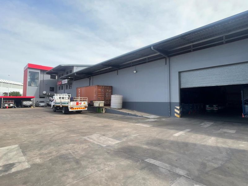 Industrial warehouse exterior featuring a large concrete yard, loading ramp, and a wide roller shutter door for efficient logistics and access.