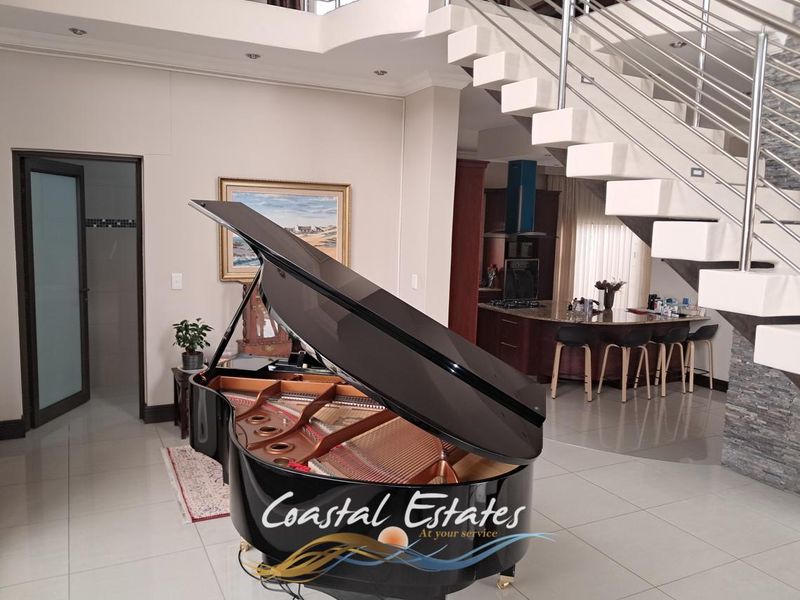 Spacious open-plan living area featuring a striking floating staircase with stainless steel balustrades, tiled flooring, and a modern kitchen with a central island.