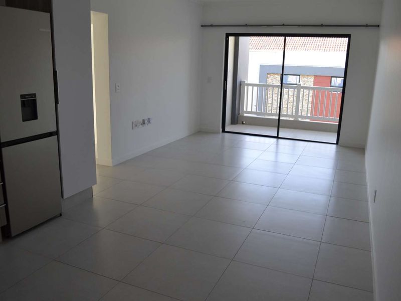 An open-plan living area featuring neutral tiled flooring, modern cabinetry, and a sliding glass door leading to a private balcony.
