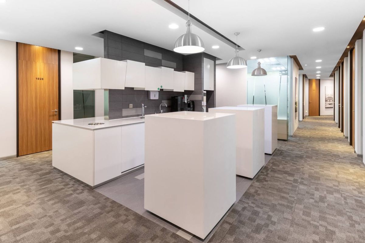 Modern office kitchenette featuring sleek white cabinetry, stone countertops, and integrated lighting, seamlessly integrated into a professional workspace hallway.