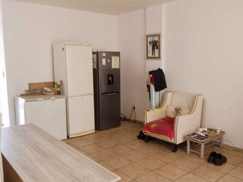 A functional kitchen area featuring tiled flooring and plain white walls, currently utilized with various appliances and furniture.