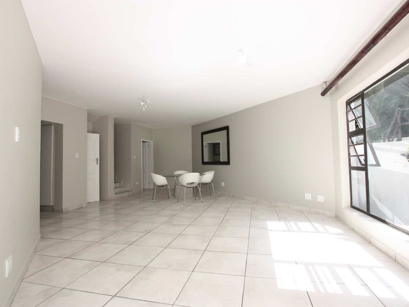 Spacious open-plan living and dining area featuring neutral tiled flooring, large windows providing natural light, and direct access to the staircase.