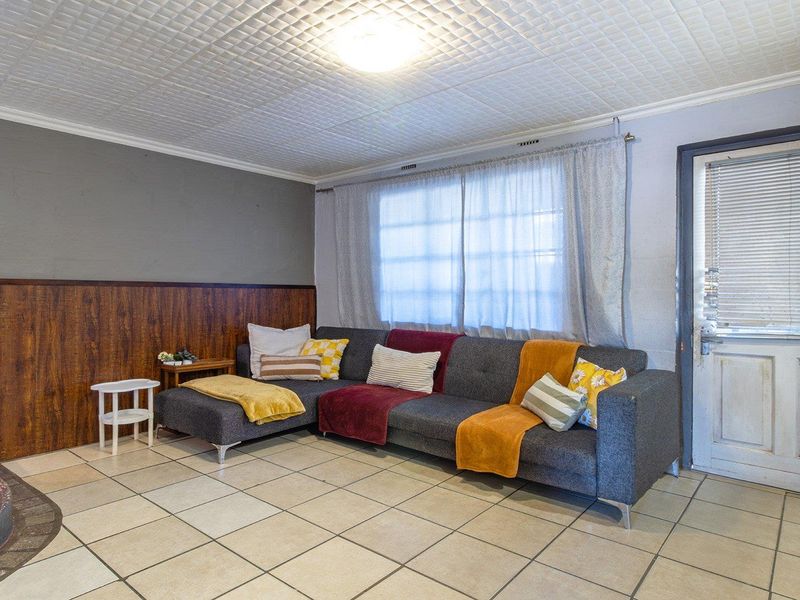 Living room featuring tiled flooring, wood-look wall paneling, textured ceiling tiles, and an external door with integrated blinds.