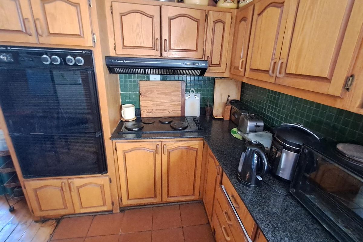 A dated kitchen featuring traditional timber cabinetry, dark granite-style countertops, a built-in oven, and a black electric hob with an integrated extractor fan.