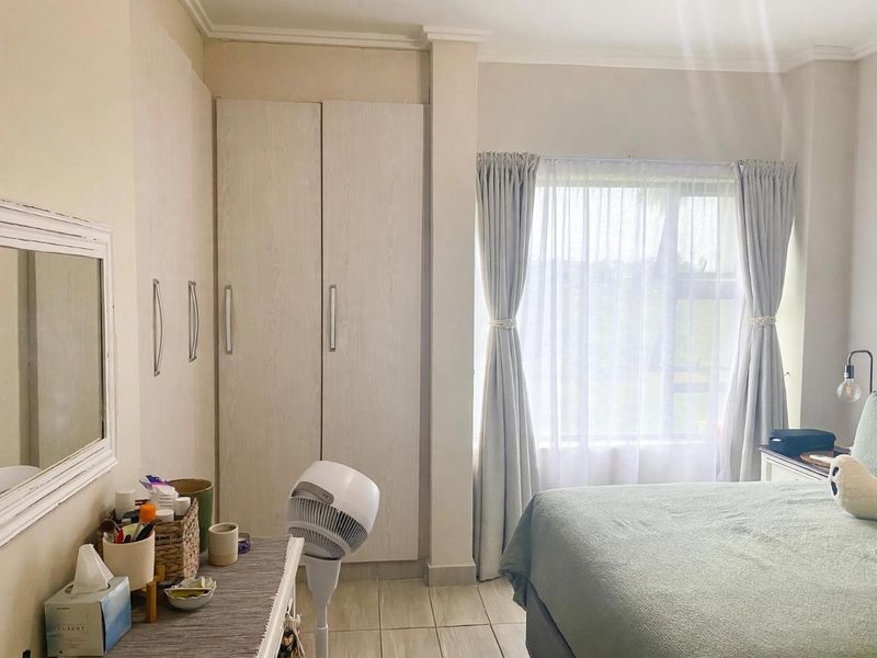 A well-lit bedroom featuring neutral-toned built-in cupboards, tiled flooring, and a window with soft drapery, offering a clean and functional living space.