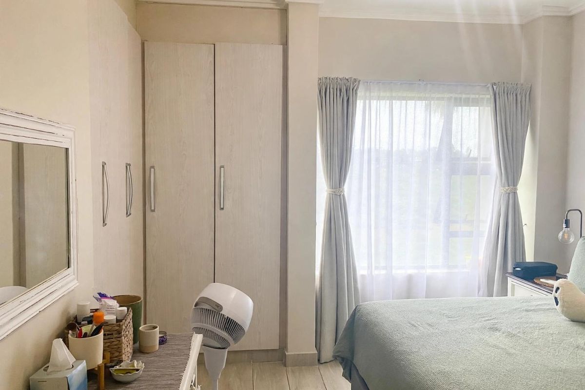 A well-lit bedroom featuring neutral-toned built-in cupboards, tiled flooring, and a window with soft drapery, offering a clean and functional living space.