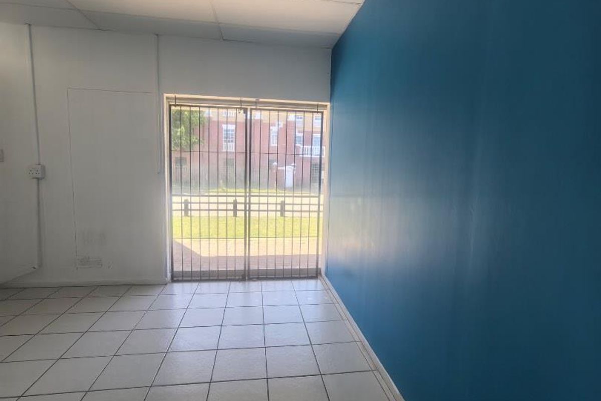 An empty interior space featuring tiled flooring, a blue accent wall, and a secure metal gate leading to the exterior.