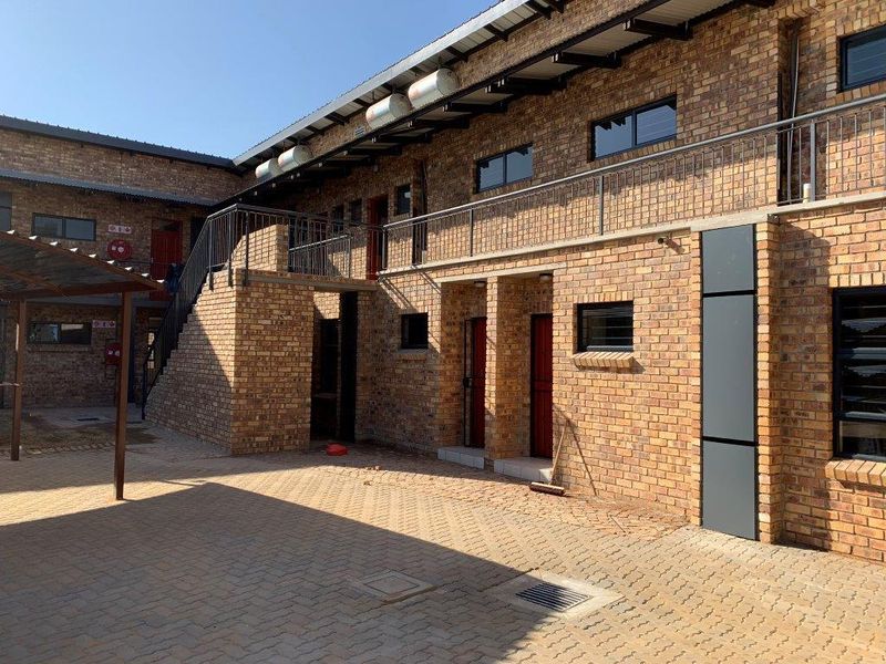 A view of the apartment complex exterior featuring face brick construction, an external staircase, metal balustrades, and a paved courtyard area.