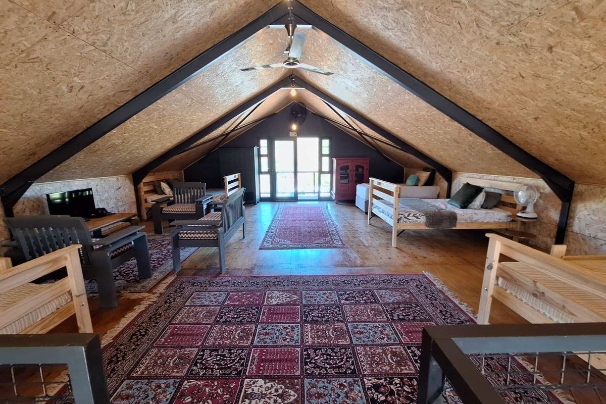 Spacious open-plan loft bedroom featuring exposed steel beams, OSB panel vaulted ceilings, and timber flooring with access to a balcony.