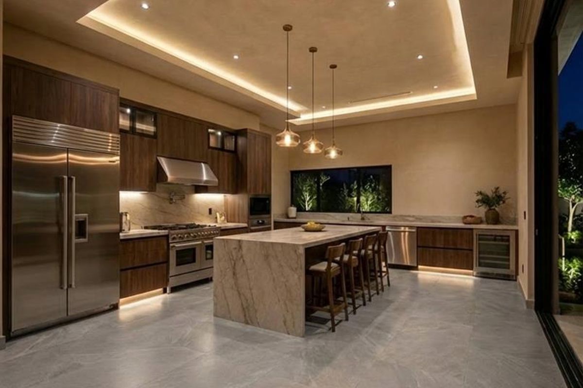 Modern luxury kitchen featuring a large stone island, high-end stainless steel appliances, custom cabinetry, and sophisticated recessed and cove lighting.