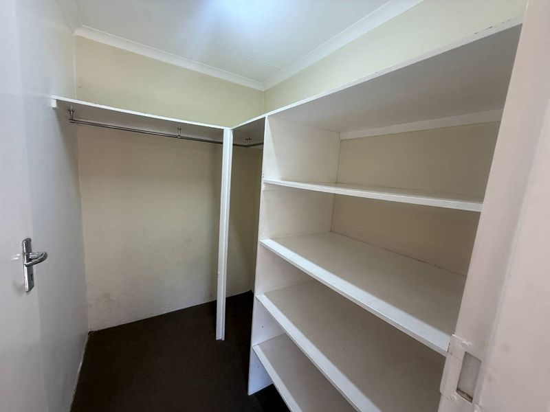A walk-in storage or dressing area featuring built-in white shelving units and metal hanging rails, providing functional storage space.