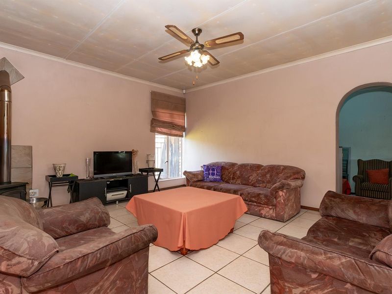 Spacious living room featuring tiled flooring, a ceiling fan, and a built-in wood-burning stove, providing a functional base for renovation.