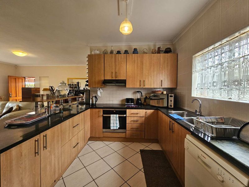 Functional kitchen featuring wood-look laminate cabinetry, granite countertops, built-in oven, electric hob, and tiled flooring with a view into the adjacent living area.