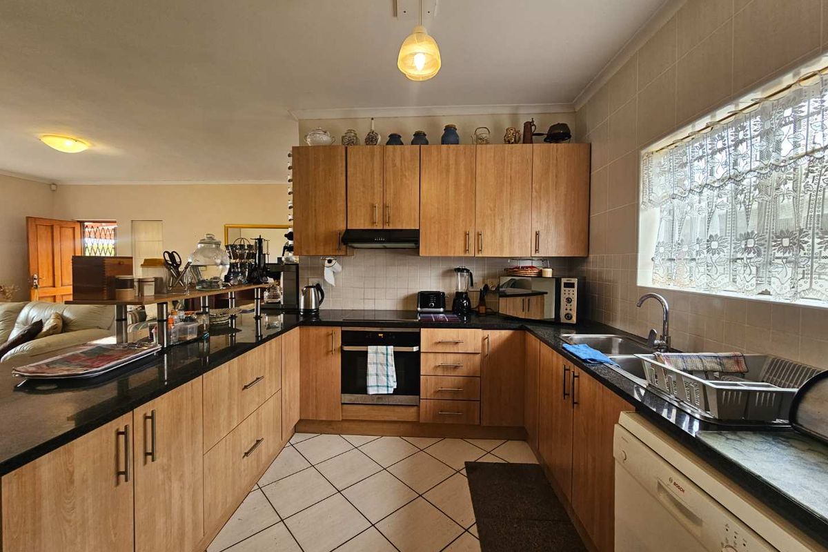 Functional kitchen featuring wood-look laminate cabinetry, granite countertops, built-in oven, electric hob, and tiled flooring with a view into the adjacent living area.