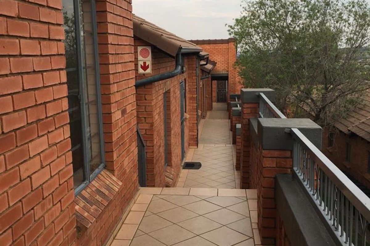 An exterior walkway featuring red brick walls, tiled flooring, and metal railings, providing access to apartment units.